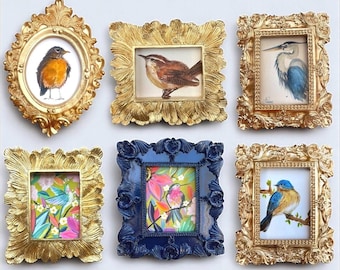May include: A collection of six ornate picture frames arranged in two rows. Four frames are gold with intricate carvings, one is a rectangular gold frame with leaf-like textures, and one is a dark blue frame. The frames contain bird paintings.