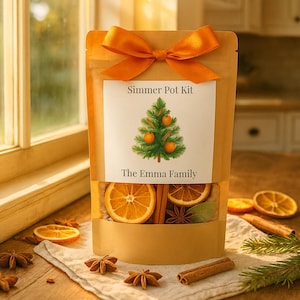 May include: A tan pouch containing a simmer pot kit, topped with an orange ribbon. The label features a Christmas tree illustration with oranges and the text Simmer Pot Kit and The Emma Family. Dried orange slices and cinnamon sticks are visible.