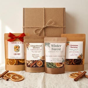 May include: A gift set featuring a brown cardboard box tied with twine and four stand-up pouches labeled Clark Party, Gingerbread Kitchen, Winter Forest, and Christmas Morning. Each pouch contains dried fruit, spices, and herbs for a simmer pot kit.