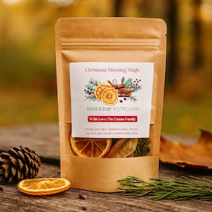 May include: A brown kraft paper pouch containing stovetop potpourri. The label reads Christmas Morning Magic, STOVETOP POTPOURRI, With Love, The Emma Family, and lists ingredients including orange peel slice, cinnamon stick, cloves, bay leaf, pine needles, dried cranberries.