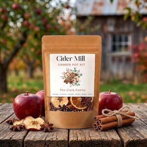 May include: A brown paper pouch labelled Cider Mill Simmer Pot Kit The Clark Family containing dried orange slices, apple slices, cinnamon sticks, and cloves, with two red apples and a bundle of cinnamon sticks tied with twine on a wooden surface.