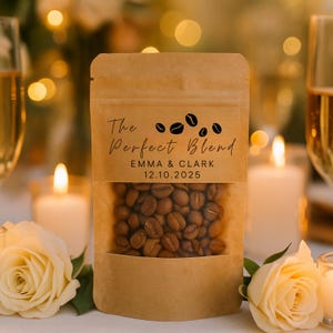 Może przedstawiać: Brązowa papierowa torebka na kawę z przezroczystym okienkiem, ukazującym ziarna kawy. Na torebce napis "The Perfect Blend", imiona "EMMA & CLARK" i data "12.10.2025". W tle świece i kwiaty.