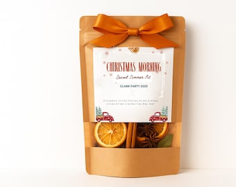 May include: A brown paper pouch with a burnt orange ribbon bow at the top. The label reads CHRISTMAS MORNING Spiced Simmer Kit CLARK PARTY 2025 with illustrations of red plaid trucks. A clear window reveals dried orange slices, cinnamon sticks, and star anise.