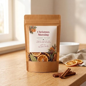 May include: A brown kraft paper pouch containing a Christmas Morning simmer pot kit. The label features text, illustrations of dried orange slices, and a clear window showing dried orange slices, cinnamon sticks, cloves, and bay leaves inside.