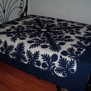 May include: A navy blue and white Hawaiian quilt with a floral pattern. The quilt is made of cotton and is hand-stitched. It is a traditional Hawaiian quilt and is a beautiful example of Hawaiian craftsmanship.