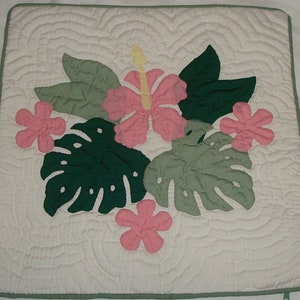 May include: A white quilted pillow cover with a green and pink floral design. The design features large green leaves, pink hibiscus flowers, and smaller pink flowers.
