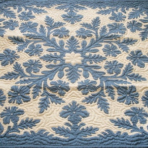 May include: A blue and white quilted throw blanket with a floral pattern. The blanket is made of cotton and is perfect for adding a touch of elegance to any room.