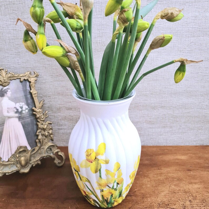 Spring Daffodils glass vase, A beautiful glass vase which has been decoupaged with vibrant yellow spring daffodils all around the vase creating a cheerful and uplifting display. set against a hand painted white chalk paint background giving it a rustic feel with natural twine tied around the vase. Height 20 cm width 11 cm