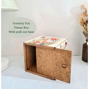 May include: Wooden tissue box with a pull-out base. The top of the box features a colorful illustration of a fox in a field. The text "Country Fox Tissue Box With pull-out base" is printed on the image.