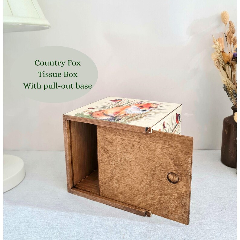 May include: Wooden tissue box with a pull-out base. The top of the box features a colorful illustration of a fox in a field. The text "Country Fox Tissue Box With pull-out base" is printed on the image.