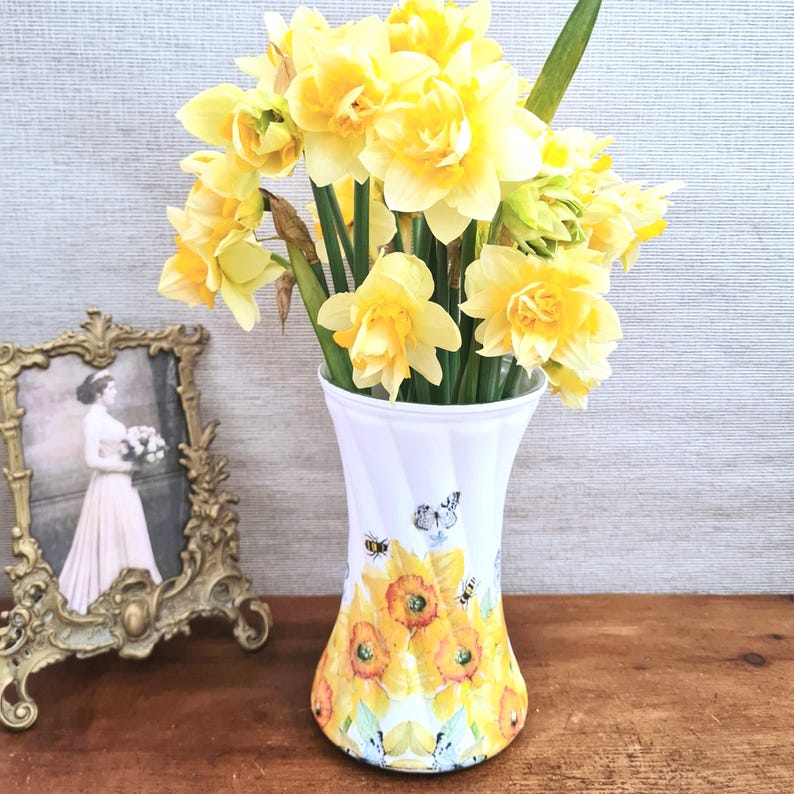 Spring daffodils tulip shaped glass vase, A pretty glass vase decoupaged with vibrant yellow daffodils with butterflies and bees amongst the flowers adding a touch of charm. against a hand painted in white chalk paint background giving a lovely rustic country feel with natural twine tied around the neck of the vase height 20 cm width 14 cm sealed to protect