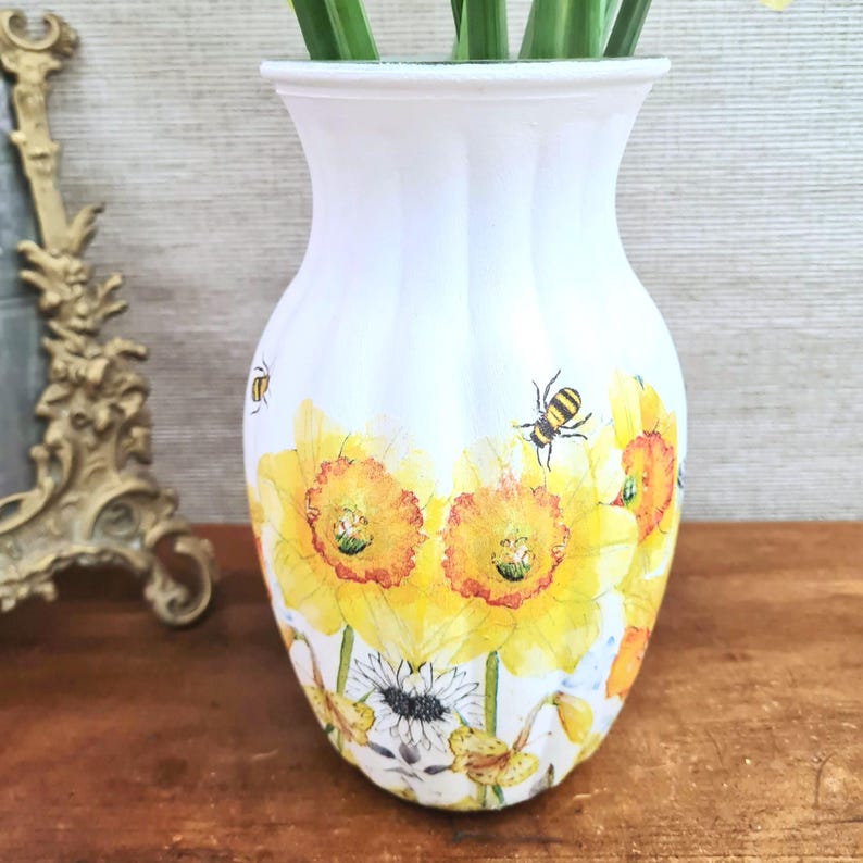Spring daffodils tulip shaped glass vase, A pretty glass vase decoupaged with vibrant yellow daffodils with butterflies and bees amongst the flowers adding a touch of charm. against a hand painted in white chalk paint background giving a lovely rustic country feel with natural twine tied around the neck of the vase height 20 cm width 14 cm sealed to protect