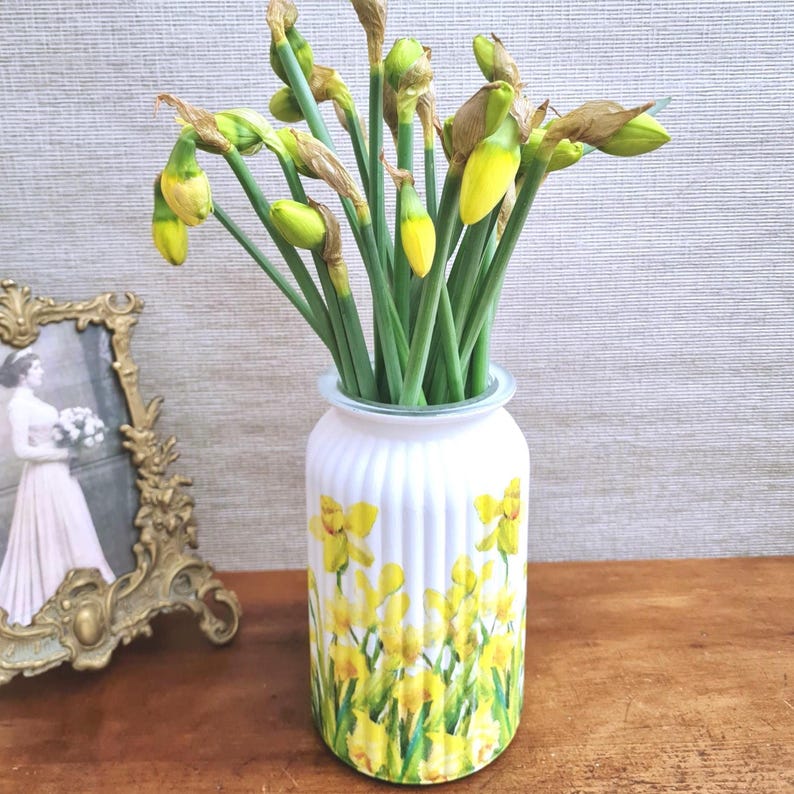 Spring Daffodils glass vase, A beautiful glass vase which has been decoupaged with vibrant yellow spring daffodils all around the vase creating a cheerful and uplifting display. set against a hand painted white chalk paint background giving it a rustic feel with natural twine tied around the vase. Height 20 cm width 11 cm