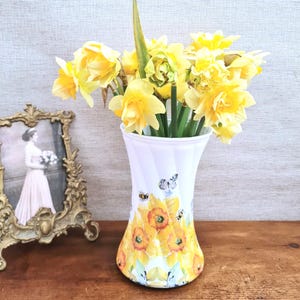 Spring daffodils tulip shaped glass vase, A pretty glass vase decoupaged with vibrant yellow daffodils with butterflies and bees amongst the flowers adding a touch of charm. against a hand painted in white chalk paint background giving a lovely rustic country feel with natural twine tied around the neck of the vase height 20 cm width 14 cm sealed to protect