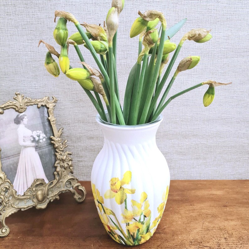 Spring Daffodils glass vase, A beautiful glass vase which has been decoupaged with vibrant yellow spring daffodils all around the vase creating a cheerful and uplifting display. set against a hand painted white chalk paint background giving it a rustic feel with natural twine tied around the vase. Height 20 cm width 11 cm