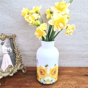 Spring daffodils tulip shaped glass vase, A pretty glass vase decoupaged with vibrant yellow daffodils with butterflies and bees amongst the flowers adding a touch of charm. against a hand painted in white chalk paint background giving a lovely rustic country feel with natural twine tied around the neck of the vase height 20 cm width 14 cm sealed to protect