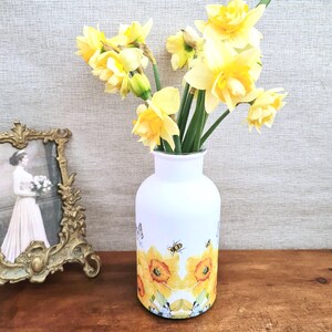 Spring daffodils tulip shaped glass vase, A pretty glass vase decoupaged with vibrant yellow daffodils with butterflies and bees amongst the flowers adding a touch of charm. against a hand painted in white chalk paint background giving a lovely rustic country feel with natural twine tied around the neck of the vase height 20 cm width 14 cm sealed to protect