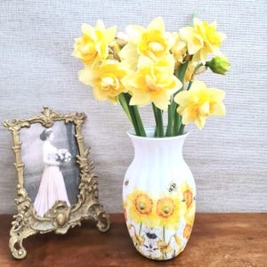 Spring daffodils tulip shaped glass vase, A pretty glass vase decoupaged with vibrant yellow daffodils with butterflies and bees amongst the flowers adding a touch of charm. against a hand painted in white chalk paint background giving a lovely rustic country feel with natural twine tied around the neck of the vase height 20 cm width 14 cm sealed to protect