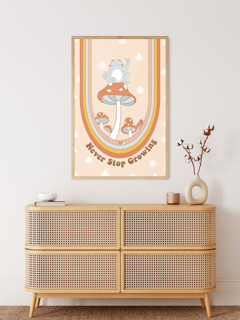 May include: A retro-style poster featuring a blue frog perched on a red mushroom. The poster has a rainbow arch and the text "Never Stop Growing" in brown lettering.