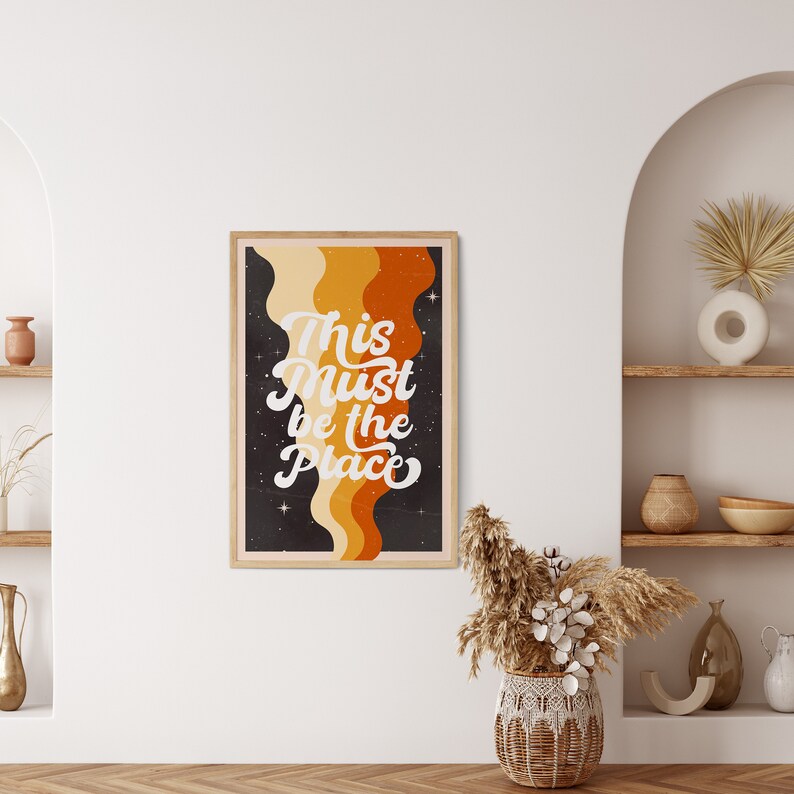 May include: A retro-style poster with a dark background and colourful wavy lines. The text "This Must Be The Place" is written in white cursive font.