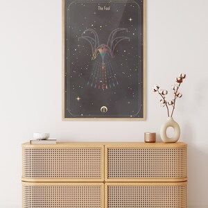 May include: A framed print of a tarot card with a black background and gold accents. The card is titled "The Fool" and features a colorful, geometric design of a figure with outstretched arms.