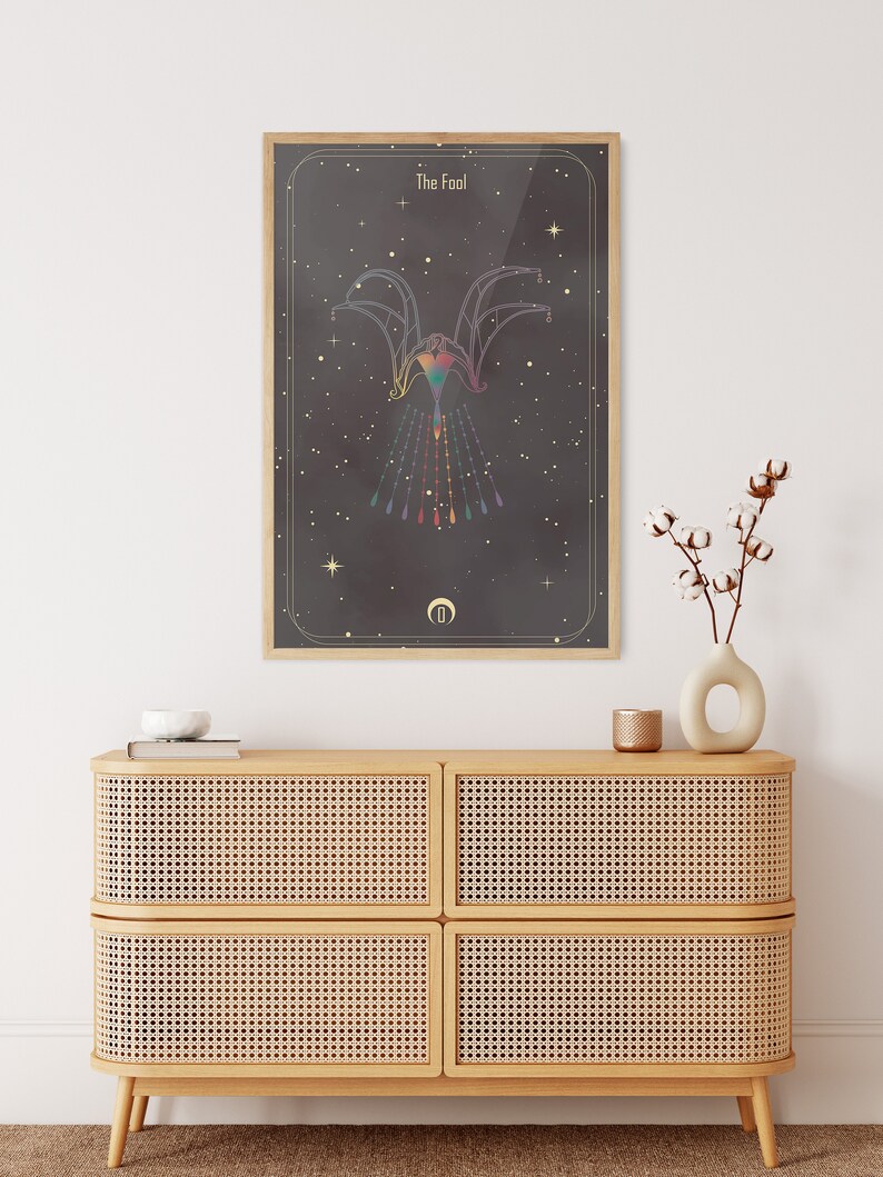 May include: A framed print of a tarot card with a black background and gold accents. The card is titled "The Fool" and features a colorful, geometric design of a figure with outstretched arms.