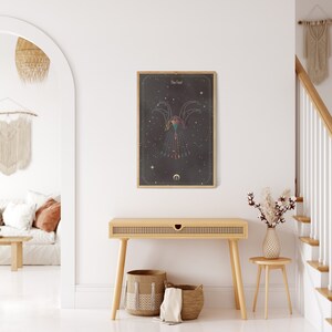 May include: A framed print with a black background and gold accents. The print features a geometric design of a bird with a crescent moon below it. The title "The Fall" is at the top of the print.