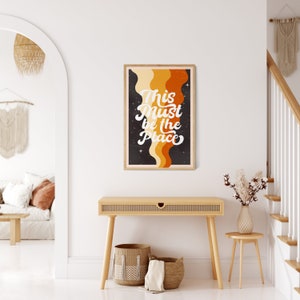 May include: A retro-style poster with a black background and colourful wavy lines. The text on the poster reads "This Must Be The Place" in a white, cursive font.