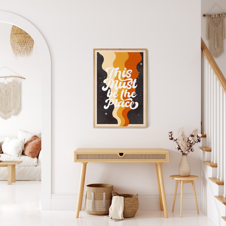 May include: A retro-style poster with a black background and colourful wavy lines. The text on the poster reads "This Must Be The Place" in a white, cursive font.