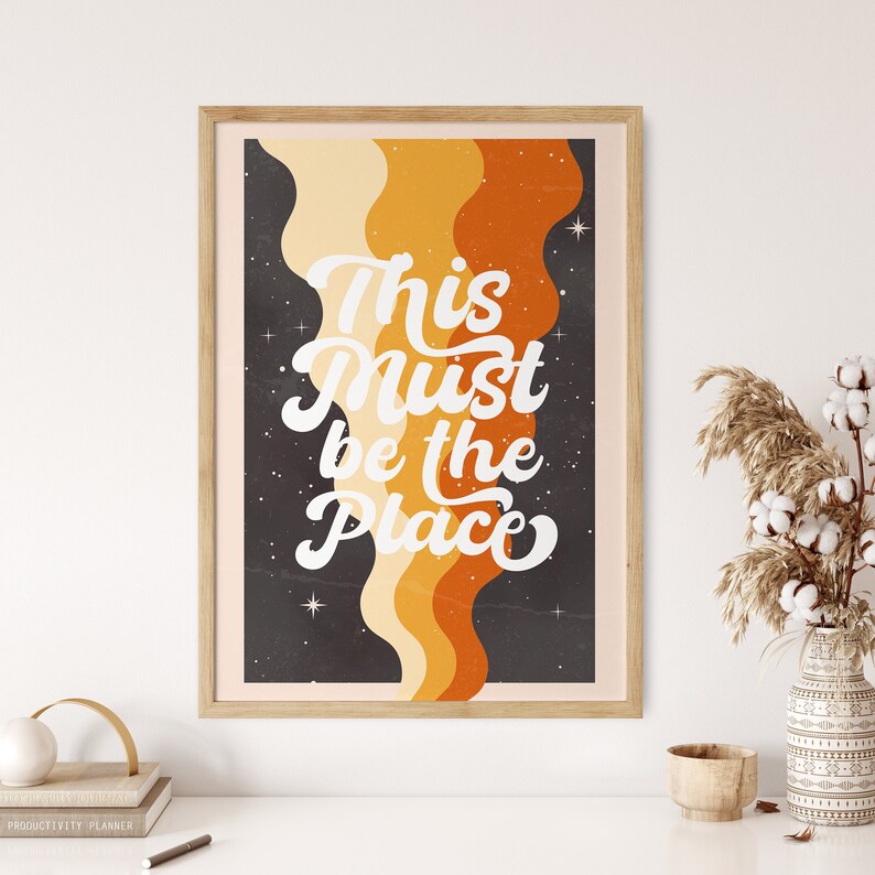May include: A retro-style poster with a black background and colourful wavy lines. The text "This Must Be The Place" is written in white cursive font.
