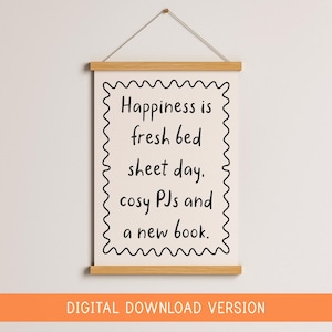 May include: A framed print with the text "Happiness is fresh bed sheet day, cosy PJs and a new book." The print has a wavy border and is suspended by a wooden bar and string. The bottom of the image reads "DIGITAL DOWNLOAD VERSION."