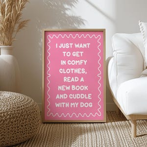May include: Pink printable wall art with a white border and white text that reads "I just want to get in comfy clothes, read a new book and cuddle with my dog."