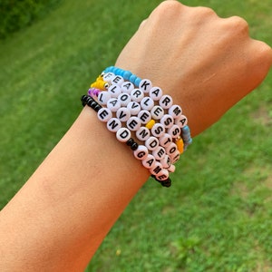 May include: A stack of colorful beaded bracelets with words spelled out on each one. The words are "Karma", "Fearless", "Love", "Even", "Game", "Stoic", and "End".