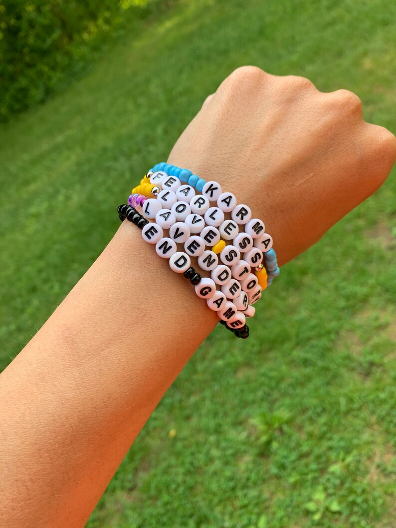 May include: A stack of colorful beaded bracelets with words spelled out on each one. The words are "Karma", "Fearless", "Love", "Even", "Game", "Stoic", and "End".