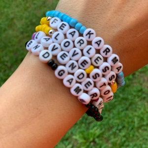 May include: A stack of colorful beaded bracelets with words spelled out on each one. The words include "Fearless", "Karma", "Love", "Lavender", "Games", "Story", and "End".