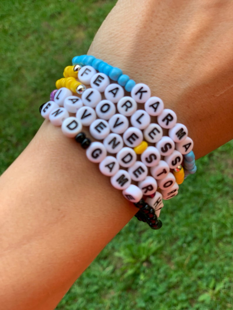 May include: A stack of colorful beaded bracelets with words spelled out on each one. The words include "Fearless", "Karma", "Love", "Lavender", "Games", "Story", and "End".