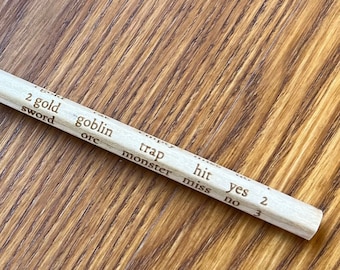 May include: A light-coloured wooden pencil with a sharpened graphite tip. The pencil has printed text including words like "gold", "goblin", and "trap". The pencil is lying on a wooden surface.