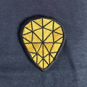 Puede incluir: Un parche de tela azul oscuro con un diseño geométrico dorado bordado.