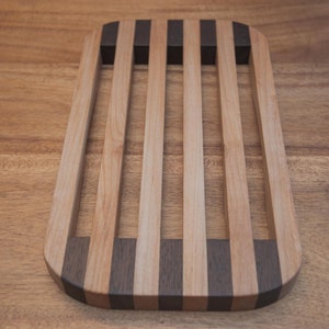 Op de afbeelding: Een houten broodkoelrek met een lichtbruine afwerking en donkerbruine strepen. Het rek heeft een rechthoekige vorm met afgeronde hoeken.