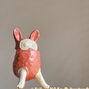 May include: A ceramic figurine of a creature with large ears, a red body, and white legs and face. The creature has large, white eyes.