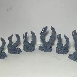 Könnte beinhalten: Satz von sieben grauen, 3D-gedruckten Miniatur-Skeletthand-Skulpturen mit erhobenen Fingern. Die Hände sind in verschiedenen Positionen angeordnet, wobei einige Finger ausgestreckt und andere gekrümmt sind.