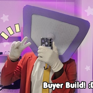 May include: A person wearing a red blazer, white gloves, and a yellow tie, holding a phone. The person is wearing a large, square-shaped headpiece with a purple border. The image includes the text "Buyer Build! :D".