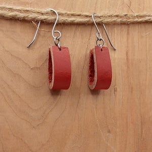 May include: A pair of red leather earrings with silver hooks. The earrings are shaped like a teardrop and are about 1 inch long.