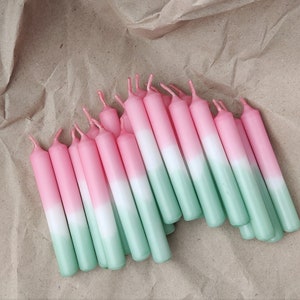 Könnte beinhalten: Ein Bündel rosa, weiß und grün ombre Geburtstagskerzen. Die Kerzen sind fächerförmig auf einem braunen Papierhintergrund angeordnet.