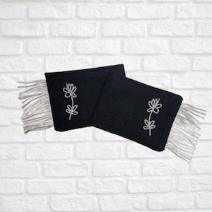May include: Two rectangular black fabric patches featuring a silver embroidered floral design on each. Both patches are finished with silver fringe trim on the outer edges, creating a decorative accent for clothing or textile projects.