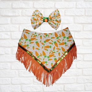 May include: A white pet bandana and bow tie set with a carrot pattern. The bandana has orange fringe and green sequins. The bow tie has a green and orange center.