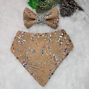 Può includere: Un bandana per cani color sabbia con paillettes e un papillon scintillante. Il bandana ha un design a forma di fuochi d'artificio con paillettes multicolori. Il papillon ha un centro di strass.