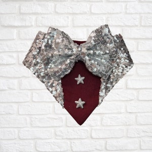 Può includere: Un papillon in tessuto bordeaux con un fiocco di paillettes argentate e due stelle argentate.