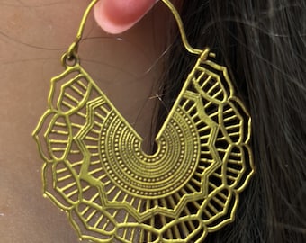 May include: Gold hoop earrings with a detailed mandala design. The earrings are made of metal and have a delicate, intricate pattern.