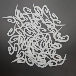 May include: A pile of white plastic curtain hooks. The hooks are designed to be used with curtain rings.